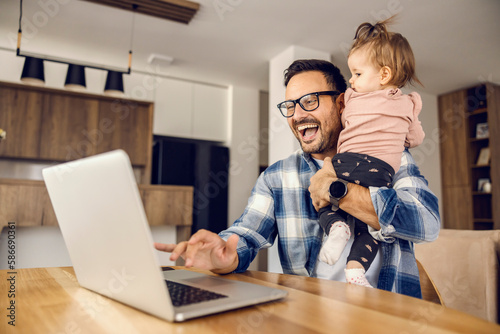 A happy father is working remotely while babysitting his baby girl. photo