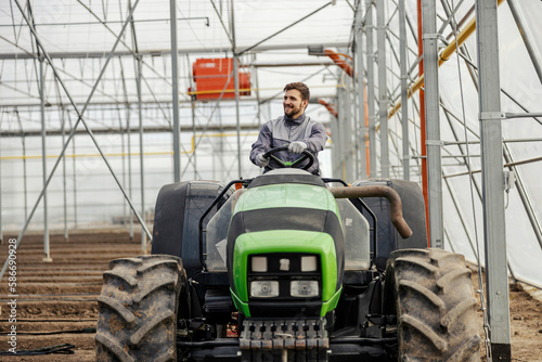 Fotografi An agronomy worker is plowing the land with tractor in hothouse.