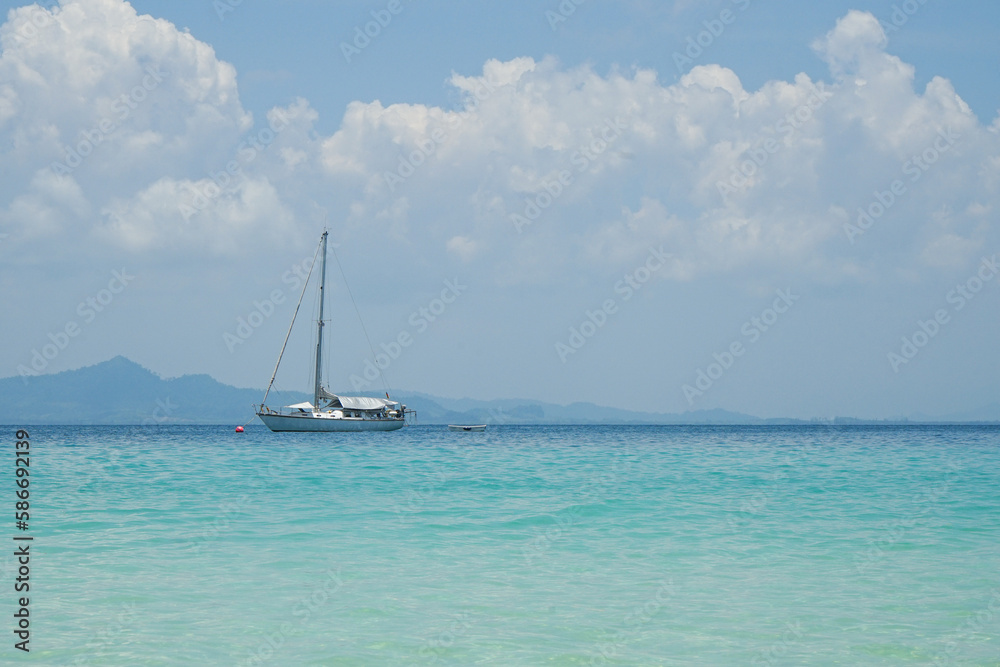 The yacht parking in the calm sea with moving paddle boat and mountain with blue sky in background