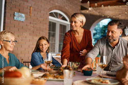 Happy woman serving food at dining table during family lunch on patio.