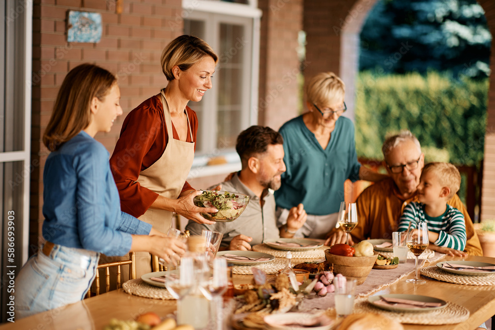 Happy woman serving food to her extended family at dining table on terrace. Happy woman serving food to her extended family at dining table on terrace.