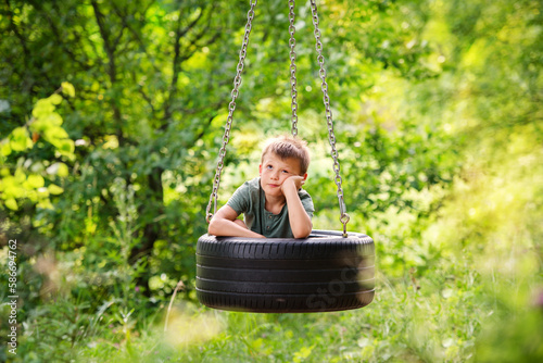 sad boy in a swing tire in the forest. Quarrel with friends, resentment, loneliness