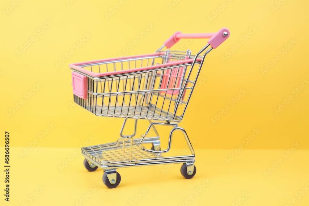 Caddie vide de supermarché à roulettes dans un fond de couleur uni jaune