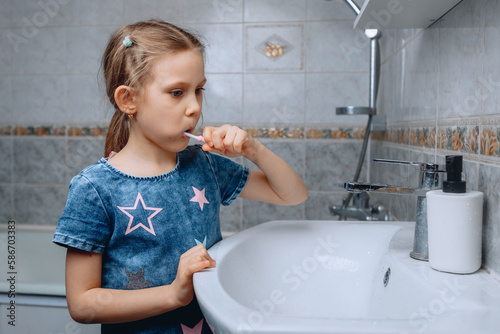 A little girl observes oral hygiene and thoroughly cleans her teeth in the bathroom next to the sink.