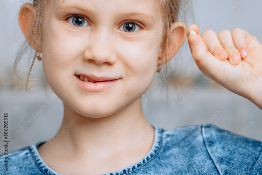 An approximate portrait of a cute little girl holding the first fallen baby tooth on a blurry bathroom background. An approximate portrait of a cute little girl holding the first fallen baby tooth on a blurry bathroom background.