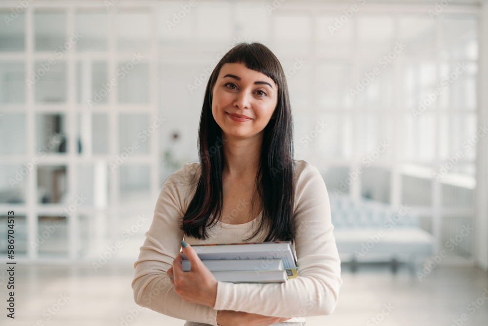 Portrait of a young beautiful woman with books in her hands in a large bright room. Beautiful brunette, young teacher or student Portrait of a young beautiful woman with books in her hands in a large bright room. Beautiful brunette, young teacher or student
