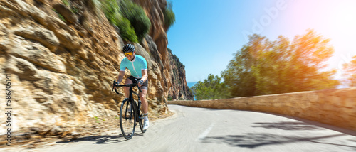 Obraz na płótnie Man Adult on a racing bike climbing the hill at mediterranean sea landscape coastal road on mallorca balearic island w salonie