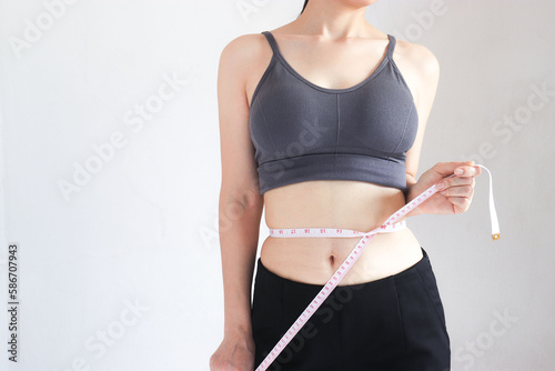 A woman measures her waist with a tape measure