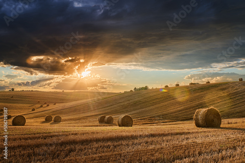 Stubble in a field with bales under a spectacular sky with clouds through which the sun's rays shine through