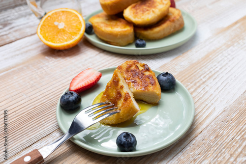 Cup piece of Torrijas, French Toast Made Of Sliced Bread, Served With Orange Topping, Glaze, Fresh Blueberries, Strawberry On Green Plate,Wooden Table.A Half Of Orange.Dessert On breakfast.Horizontal