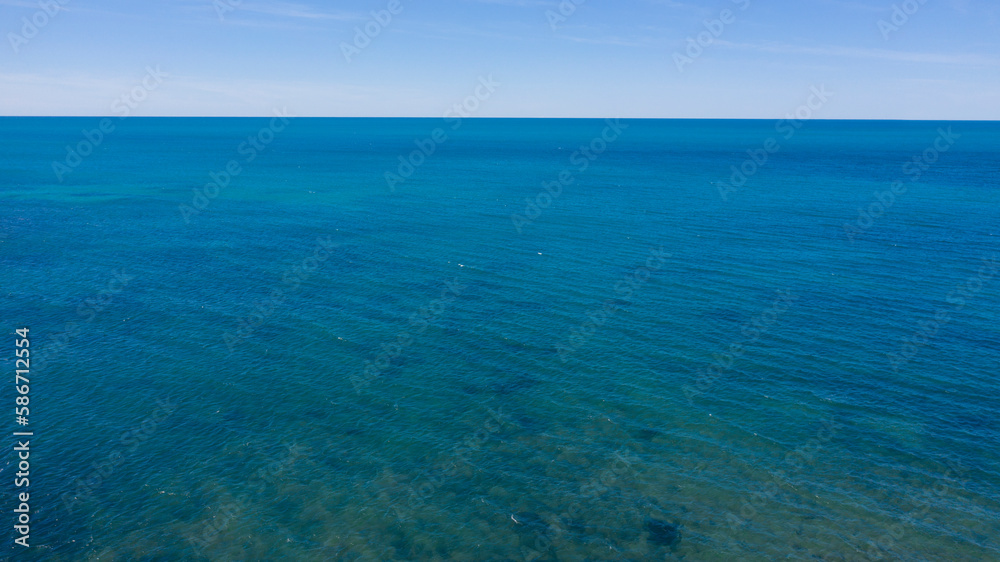 Aerial view of the blue waters of the Mediterranean Sea and specifically of the Tyrrhenian Sea from Sardinia. Sunlight is reflected on the surface of the water. Sky is on background.