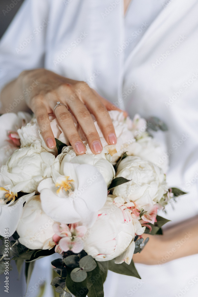 a young girl in a white wedding dress holds a bouquet of flowers and greenery with a ribbon in her hands. a bouquet of flowers piona a young girl in a white wedding dress holds a bouquet of flowers and greenery with a ribbon in her hands. a bouquet of flowers piona