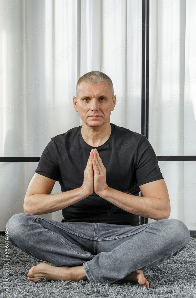 Fototapeta premium Portrait of a man who meditates in the lotus position on a yoga mat during a break at work.