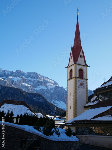 Selva Val Gardena, Bozen, Trentino Alto Adige, Italy: view of St. Mary's Parish Church's bell tower against snow covered mountains and clear blue sky 