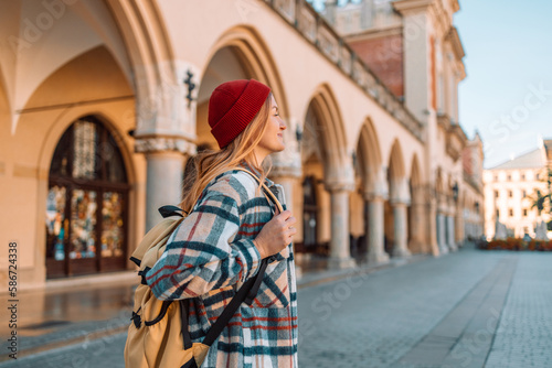 Young woman tourist in red cap with a backpack standing traveling in front of Market Square in Krakow. Travel summer tourism holiday vacation background