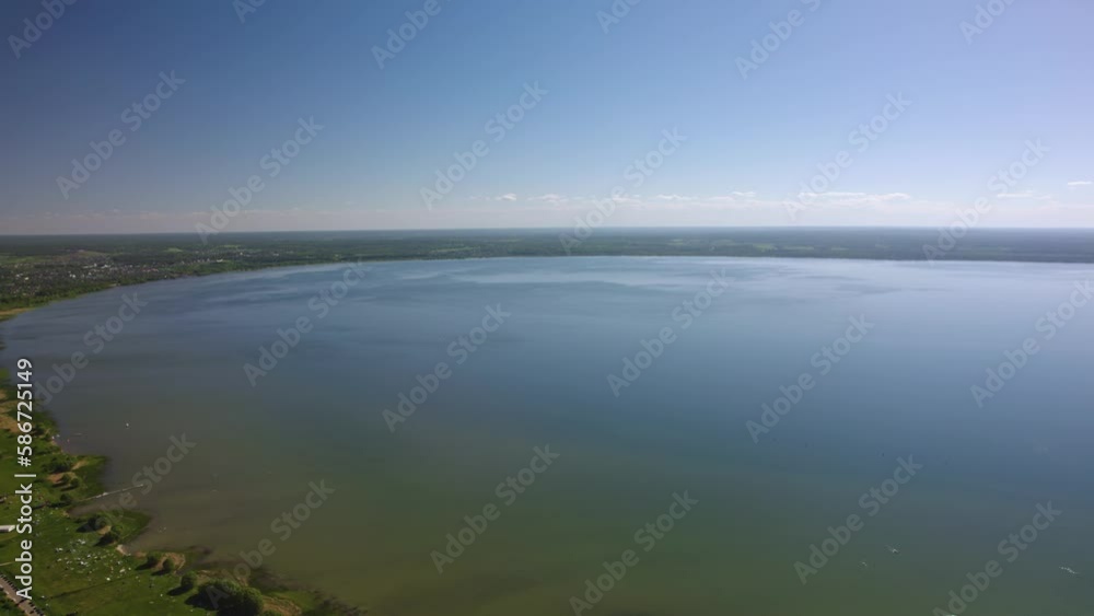 This drone video shows a beautiful lake surrounded by dense forest. The water on the lake is calm and transparent, reflecting the greenery of the trees and the blue sky. The shore of the lake is decor This drone video shows a beautiful lake surrounded by dense forest. The water on the lake is calm and transparent, reflecting the greenery of the trees and the blue sky. The shore of the lake is decor