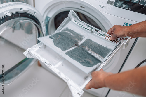 Horizontal photo of female hand taking the lint out from dirty air filter of the dyer machine 