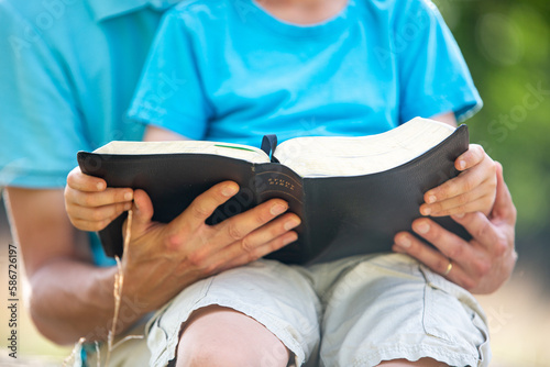 Father and young son on his lap reading the Bible together