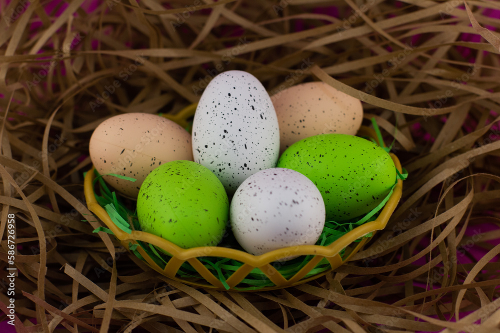 In the nest are eggs painted in different colors for the Easter holiday. Chicken eggs prepared for Easter in a wicker bird's nest on a pink background. Easter nest concept with eggs.