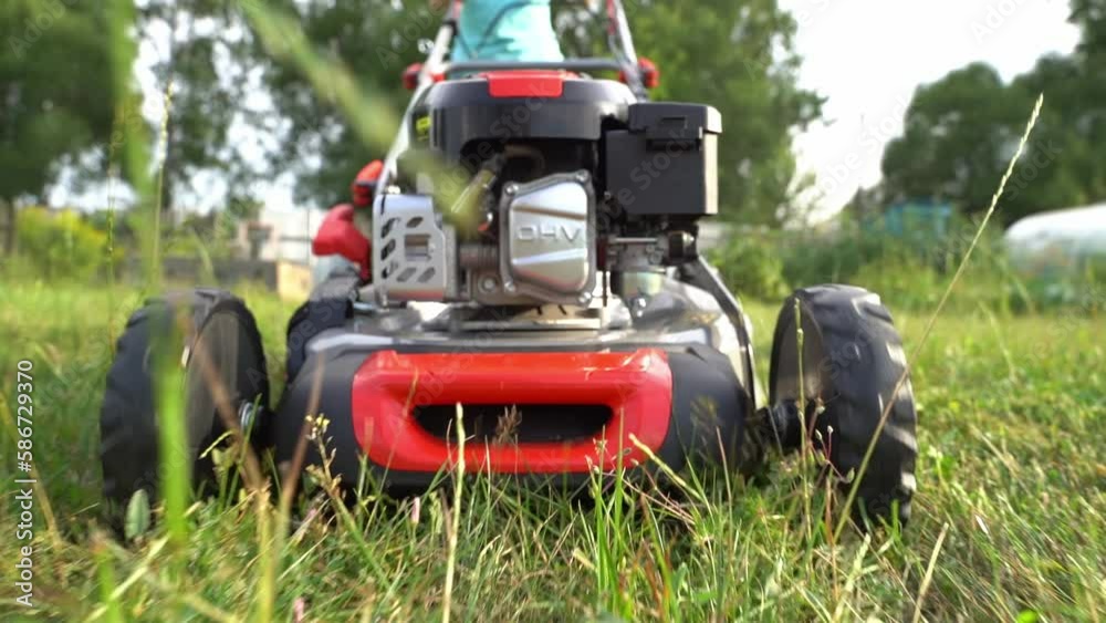 Close up shot of A man mows the grass in the backyard with an electric lawn mower. Slow motion