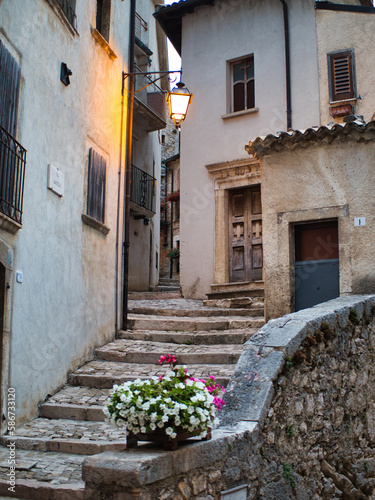 Fancy flower decorated narrow sunny street with stairs in old town in summer sunshine, Italy