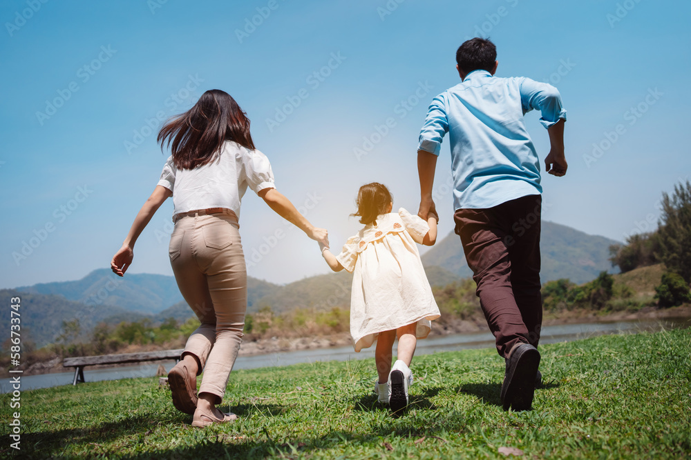Happy family in the nature travel. family on weekend playing together in the meadow with river Parents hold the child and daughter hands.health life insurance plan concept. Happy family in the nature travel. family on weekend playing together in the meadow with river Parents hold the child and daughter hands.health life insurance plan concept.