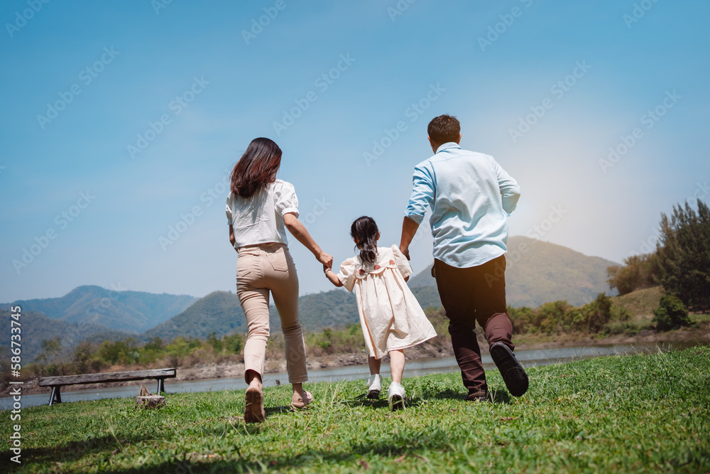 Happy family in the nature travel. family on weekend playing together in the meadow with river Parents hold the child and daughter hands.health life insurance plan concept. Happy family in the nature travel. family on weekend playing together in the meadow with river Parents hold the child and daughter hands.health life insurance plan concept.