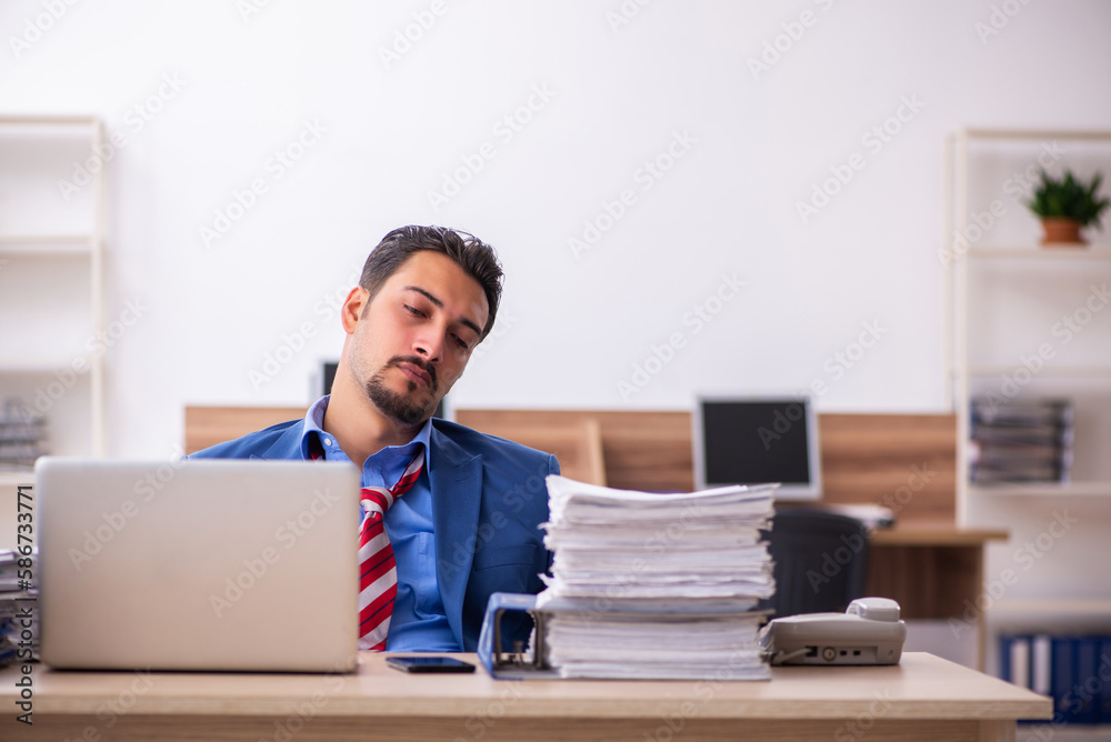 Young male employee unhappy with excessive work at workplace Young male employee unhappy with excessive work at workplace