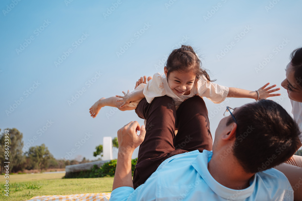 Happy family in the park on weekend. family enjoying together in the meadow with river Parents hold the daughter.health life insurance plan concept. Happy family in the park on weekend. family enjoying together in the meadow with river Parents hold the daughter.health life insurance plan concept.