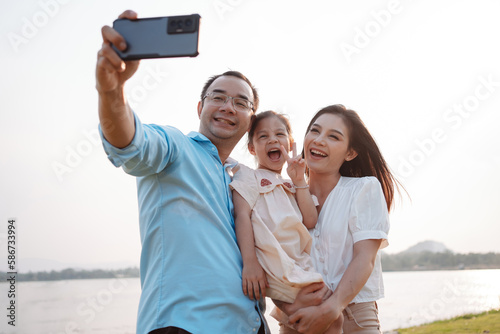 Happy family in the park on weekend. family enjoying together in the meadow with river Parents hold the daughter.health life insurance plan concept.