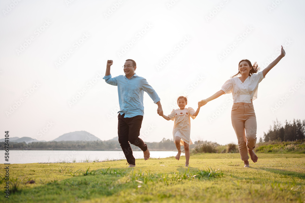 Happy family in the park sunset light. family on weekend running together in the meadow with river Parents hold the child hands.health life insurance plan concept. Happy family in the park sunset light. family on weekend running together in the meadow with river Parents hold the child hands.health life insurance plan concept.