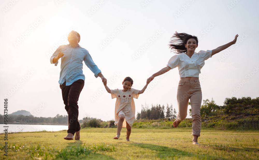 Happy family in the park sunset light. family on weekend running together in the meadow with river Parents hold the child hands.health life insurance plan concept. Happy family in the park sunset light. family on weekend running together in the meadow with river Parents hold the child hands.health life insurance plan concept.