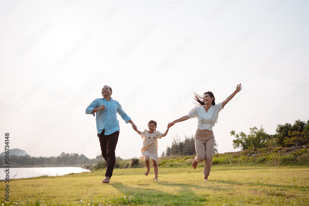 Happy family in the park sunset light. family on weekend running together in the meadow with river Parents hold the child hands.health life insurance plan concept. Happy family in the park sunset light. family on weekend running together in the meadow with river Parents hold the child hands.health life insurance plan concept.