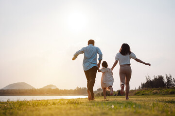 Happy family in the park sunset light. family on weekend running together in the meadow with river Parents hold the child hands.health life insurance plan concept.