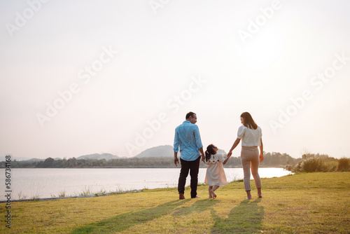 Happy family in the park sunset light. family on weekend running together in the meadow with river Parents hold the child hands.health life insurance plan concept.