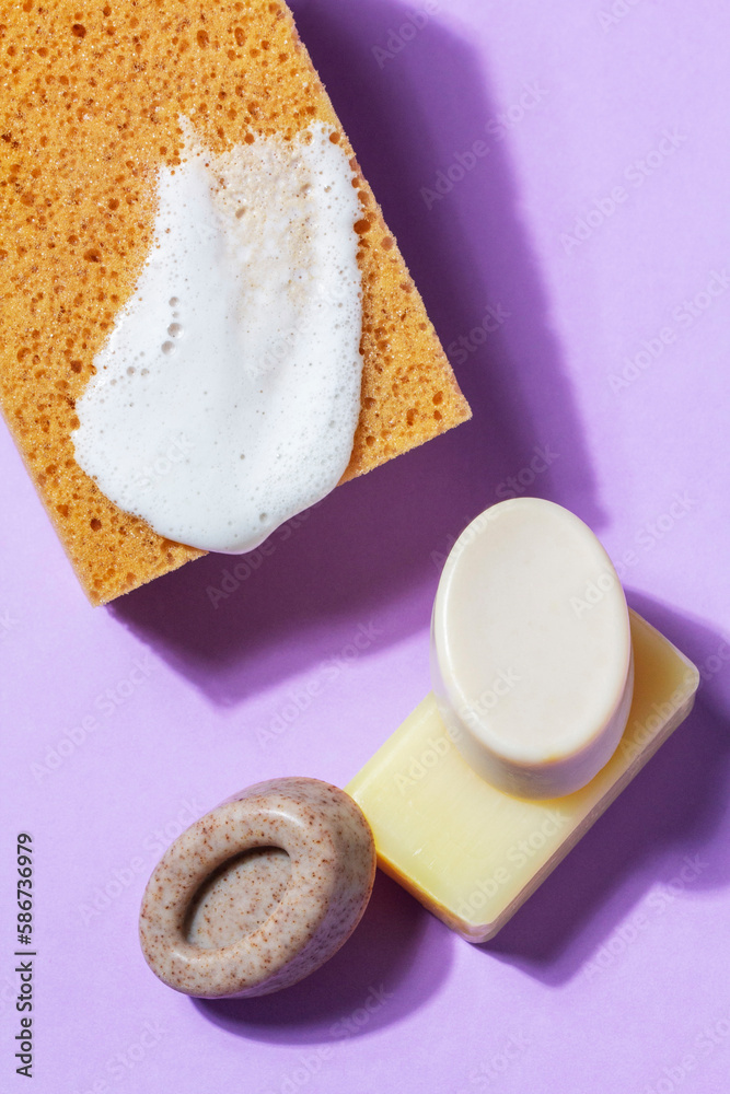 Handmade soap with the addition of coffee and wild herbs and a sponge with foam on a purple background.