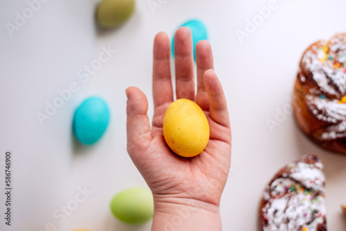 Human hand holds orange, deep yellow Easter egg on an white background with kraffin cake. photo