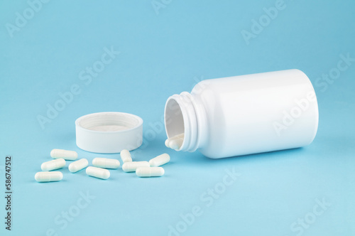 Different drugs and health supplement pills poured from a medicine white bottle health care and medical top view on colored blue background.