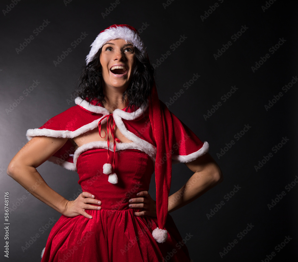 A woman in a Christmas dress shows her finger. One hand on the belt. Black background. Christmas woman. 