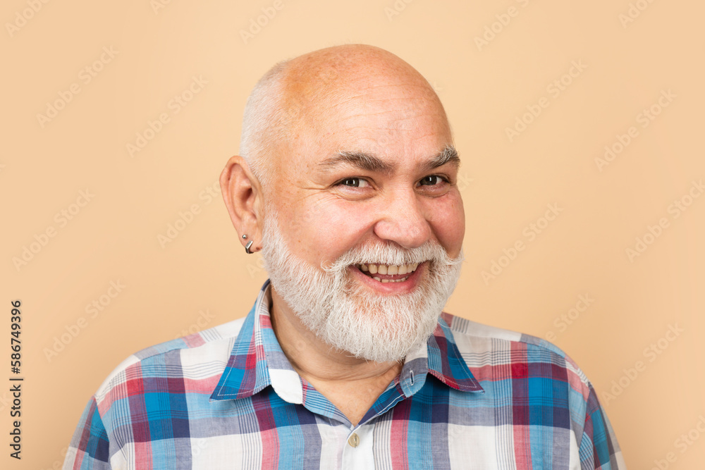 Obraz premium Happy old mature man smiling. Portrait of an bald old mature senior man with grey beard in shirt isolated on beige studio background.