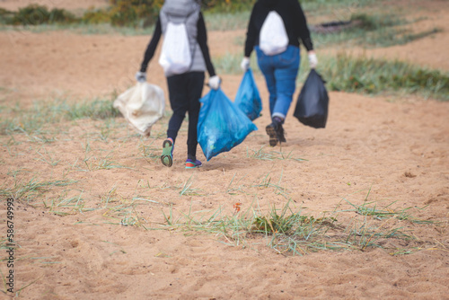 Team group of young people volunteering and participate in community work cleaning day at sandy beach, activists collecting waste, rubbish, garbage and litter in bags in the coast park together