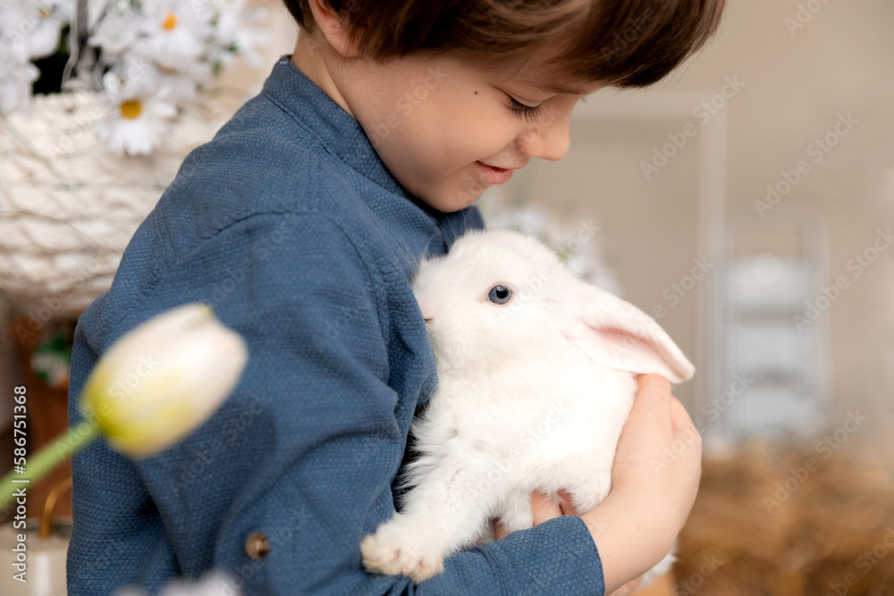 White Easter rabbit sits on the hands of a little boy, who huggs the rabbit White Easter rabbit sits on the hands of a little boy, who huggs the rabbit