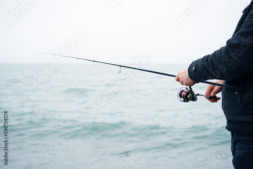 Spin fishing. Male hands hold a spinning rod against the background of the sea in spring, close-up, soft focus.