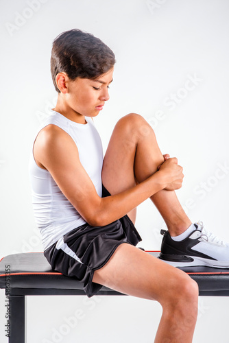 Male youth athlete runner with sports injury sitting on bench holding his hurt knee