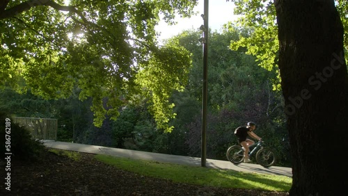 Wallpaper Mural Cyclist passes through trees at sunset. Young person riding a bike from left to right of the frame on the cycleway. The summer sunset light is filtered through the tree's leaves. Torontodigital.ca
