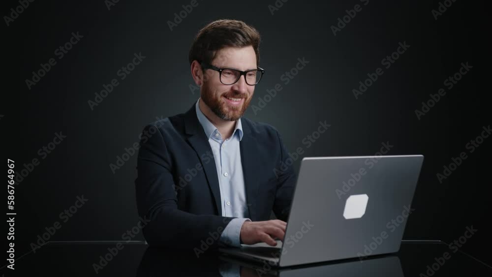 A man in a black suit working on his computer with a big smile on his face. He looks really happy. He is in a black room. High quality 4k footage A man in a black suit working on his computer with a big smile on his face. He looks really happy. He is in a black room. High quality 4k footage