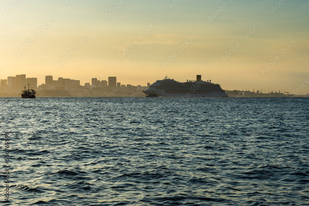 Transatlantic ship in Guanabara Bay in Rio de Janeiro, Brazil with a hill in the background. Beautiful landscape with the sea at sunset. Sailing boats and speedboats in the bay