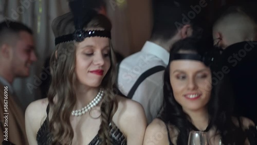 Vintage, retro Great gatsby (Roaring twenties) dressed women with smoking mouthpiece drinking champagne and dancing on a themed glamorous party photo