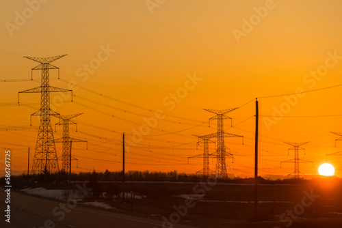 Powerlines and pylons are silhouetted against the glow of the sunset sky 