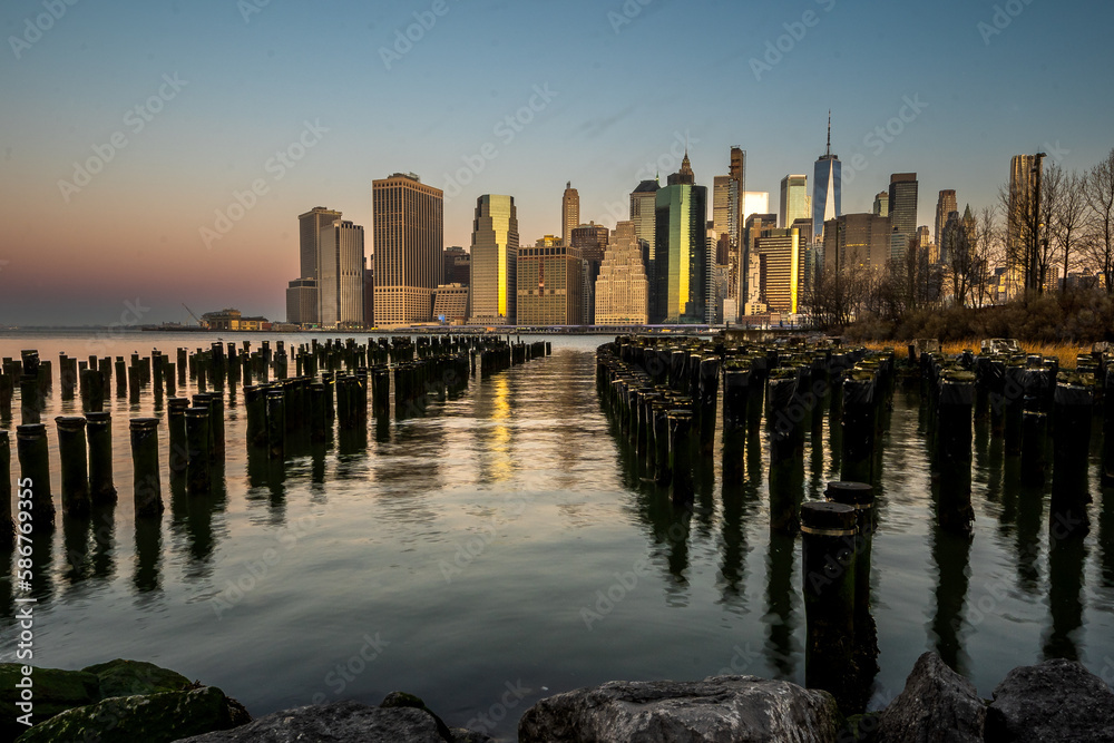 Brooklyn, NY - USA - March 26, 2023 View of the timber pilings of the former East River industrial piers at the popular Brooklyn Bridge Park, with an epic view of lower Manhattan’s skyline at sunrise.